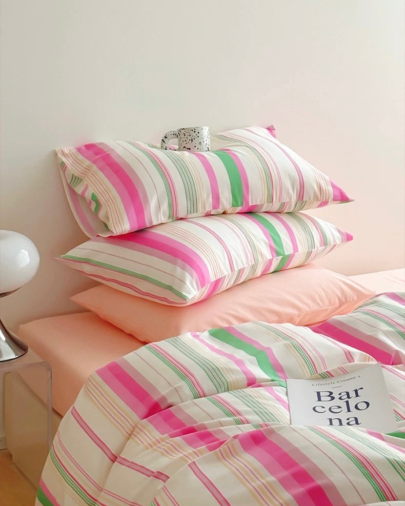 Striped bedding with pink and green patterns on a bed.
