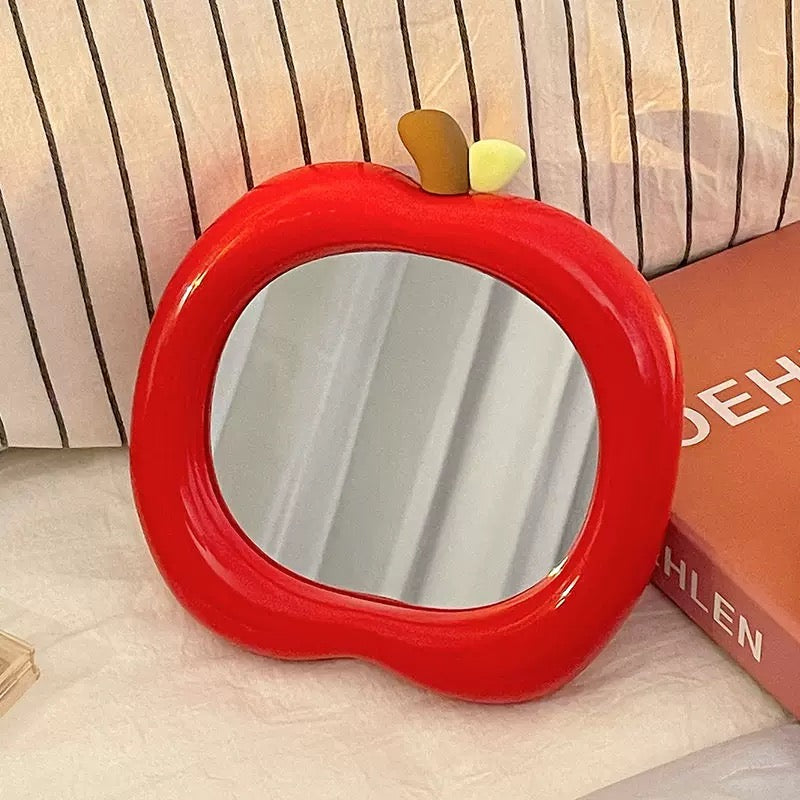 Portable apple mirror on vanity next to makeup accessories and books