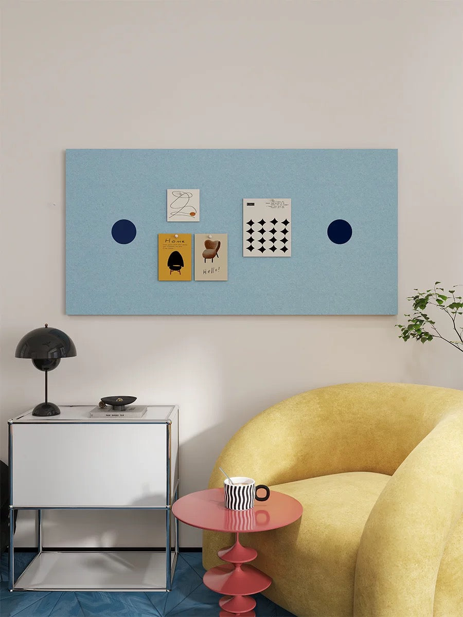 Light blue dotted bulletin board displaying prints above a white cabinet beside a yellow armchair.