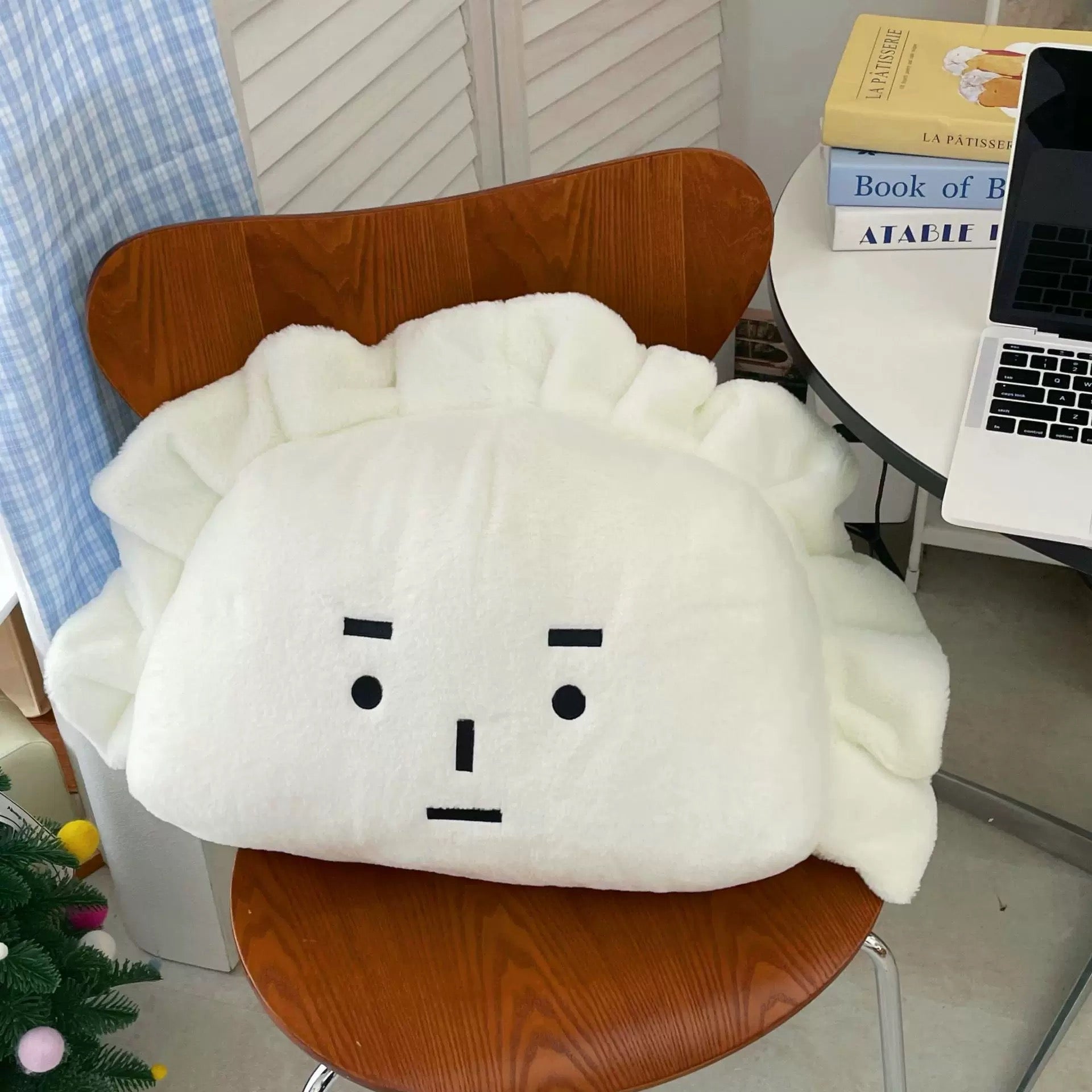 White cloud-shaped pillow with a face on a wooden chair in a room setting.