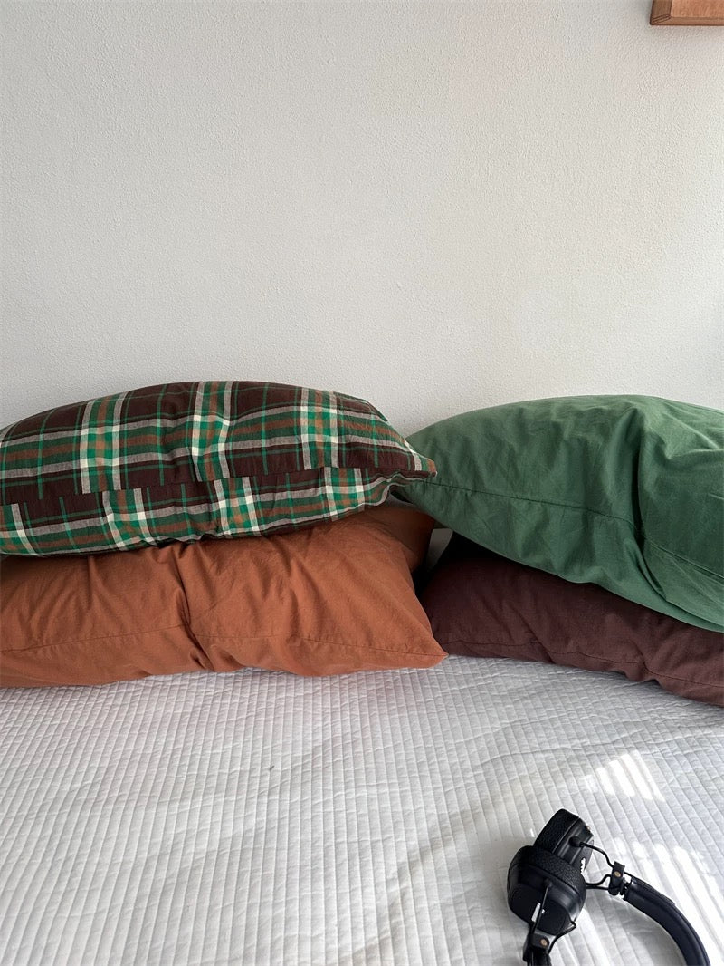 Rust orange and green pillowcases sit below a brown and green plaid design.