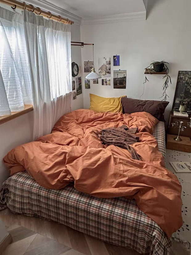 Unmade bed with orange comforter in a room with white walls and a window.
