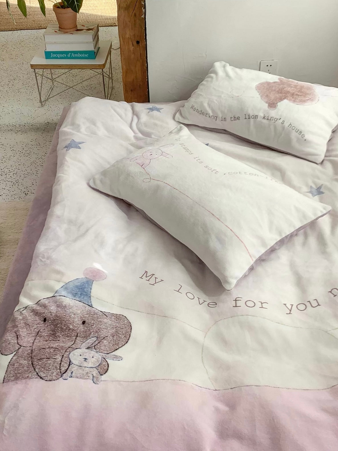 A rabbit pillowcase lies across the elephant and star cover on a purple sheet.