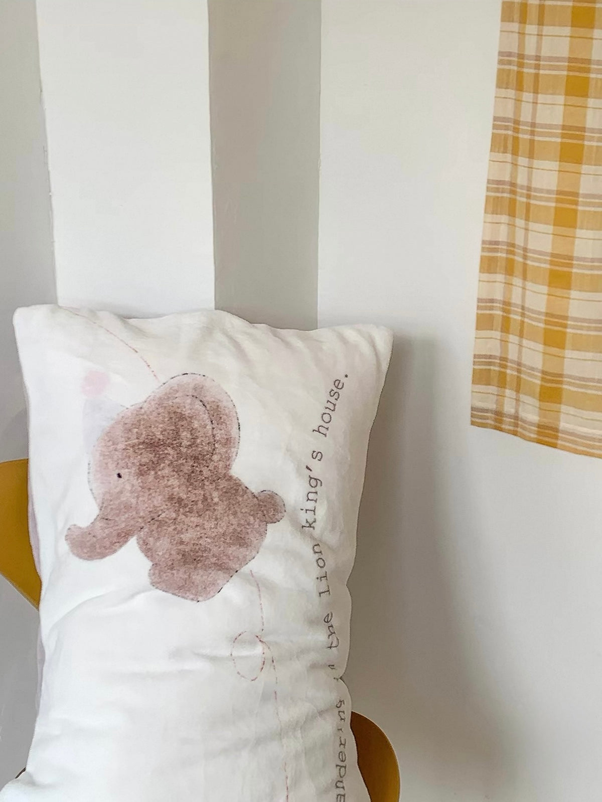 An elephant pillowcase is displayed upright on a white chair beside a yellow checked textile.