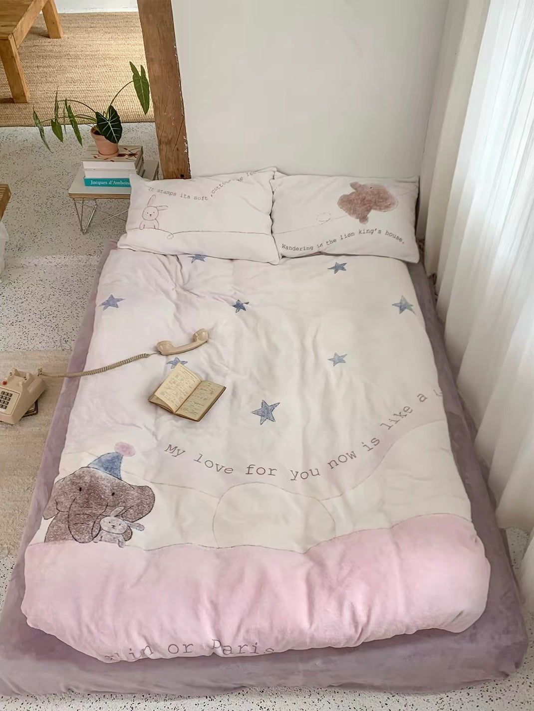 An elephant star duvet cover on a low bed has a cream center, pink border and purple sheet.