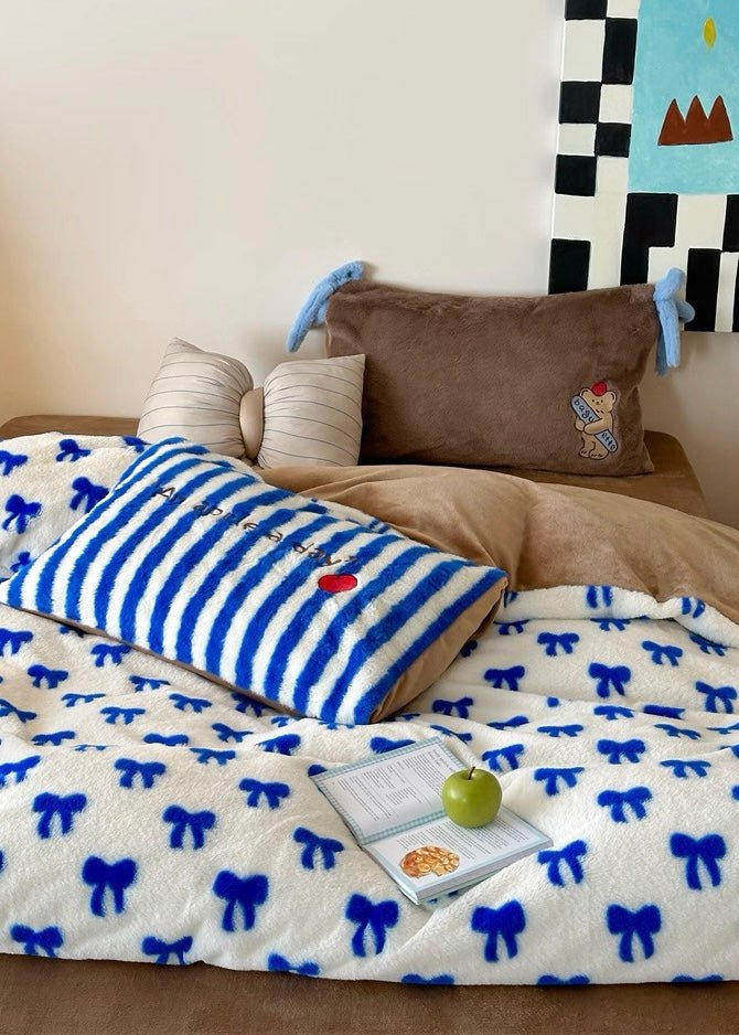 Bed with blue and white striped pillow, brown pillow, and bow-patterned comforter.