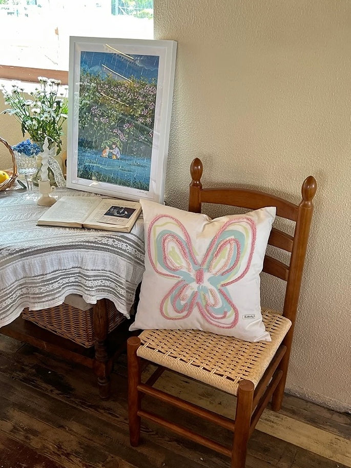 Embroidered throw pillow with a pastel butterfly and looped pink thread on a white cotton canvas cover