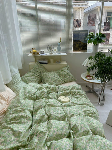 Bed with green floral bedding in a bright room with plants and decor.