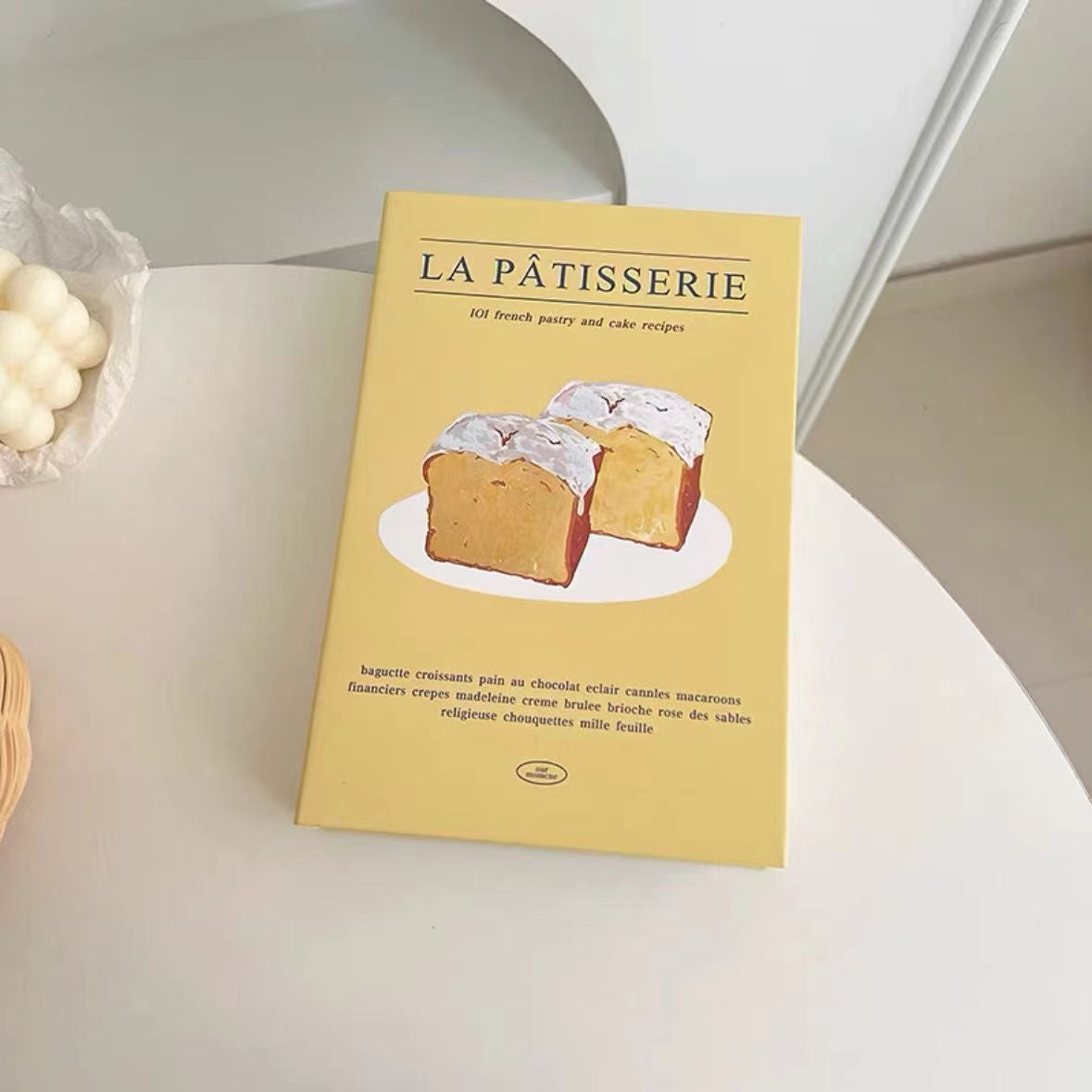 Yellow cookbook titled 'La Patisserie' on a white surface