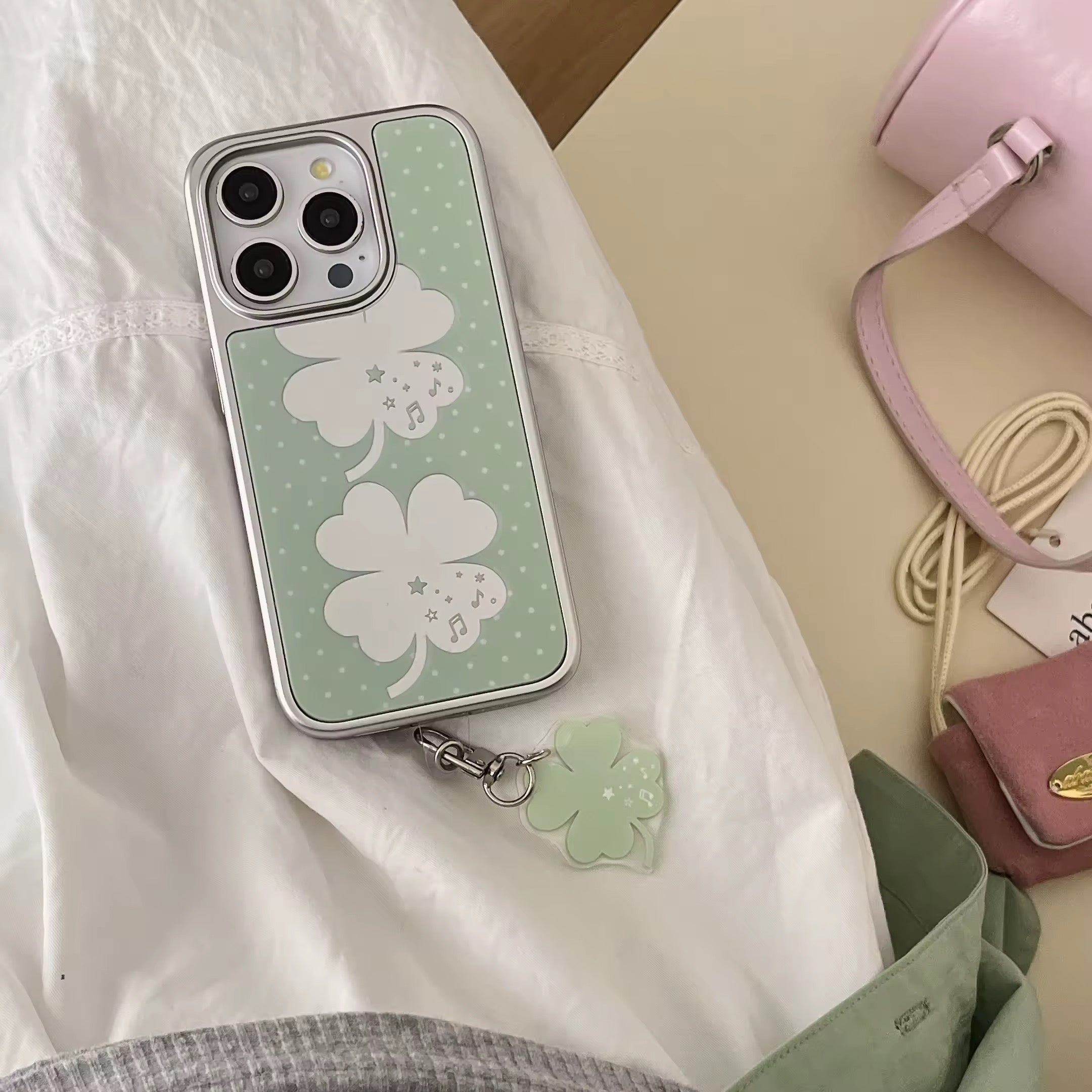 Soft girl tech accessory: green mirror clover iPhone case with matching pendant.