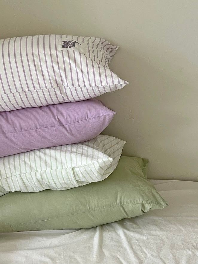 Lavender grape embroidered pillowcase resting in front of sage green and lilac pillows on a made bed.