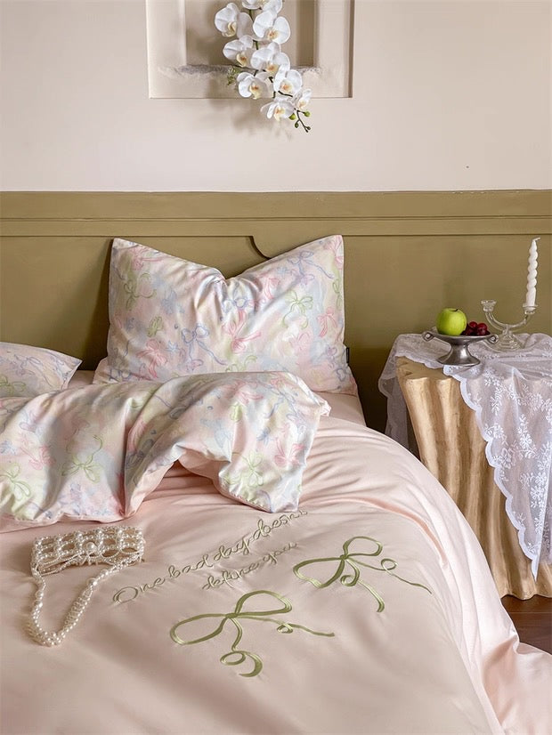Bed with pink floral bedding and embroidered design, side table with green apple and candles.