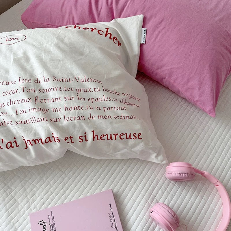 White pillow with red text on a bed with pink pillows and headphones.
