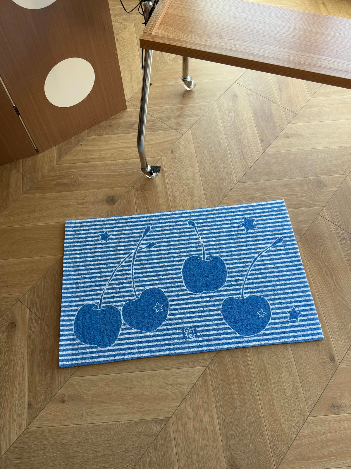 A rectangular blue and white striped mat featuring a cherry pattern, placed on a light wood herringbone floor near a wooden table.