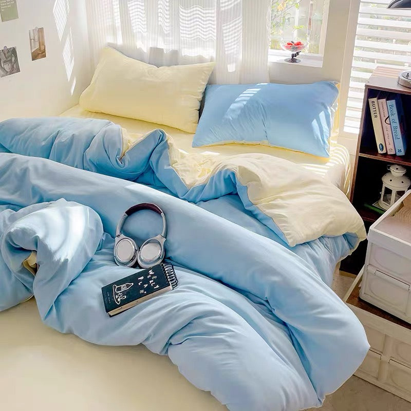 Bed with light blue bedding and yellow pillows, next to a nightstand with books.