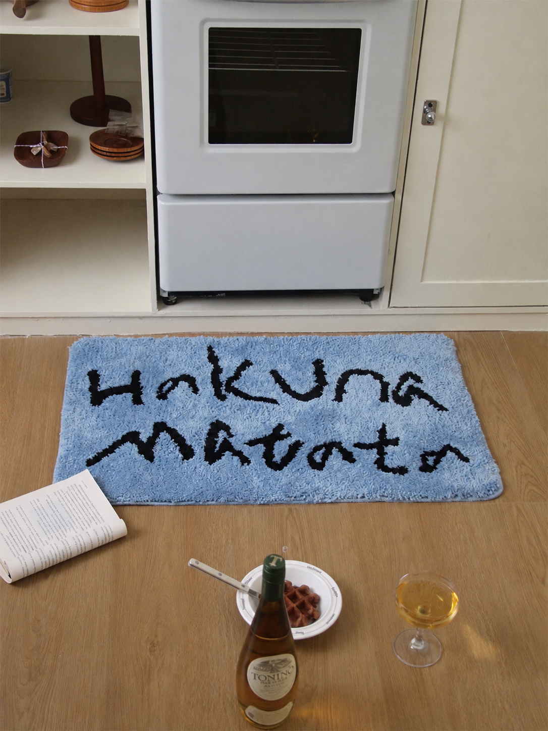 A funny bath mat in blue has black Hakuna Matata lettering and rounded corners on the kitchen floor.