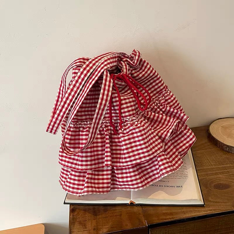 Red and white checkered bag on an open book with a wooden surface and light-colored wall background