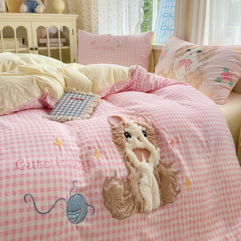 Pink checkered comforter with embroidered mouse design on a bed in a bedroom.