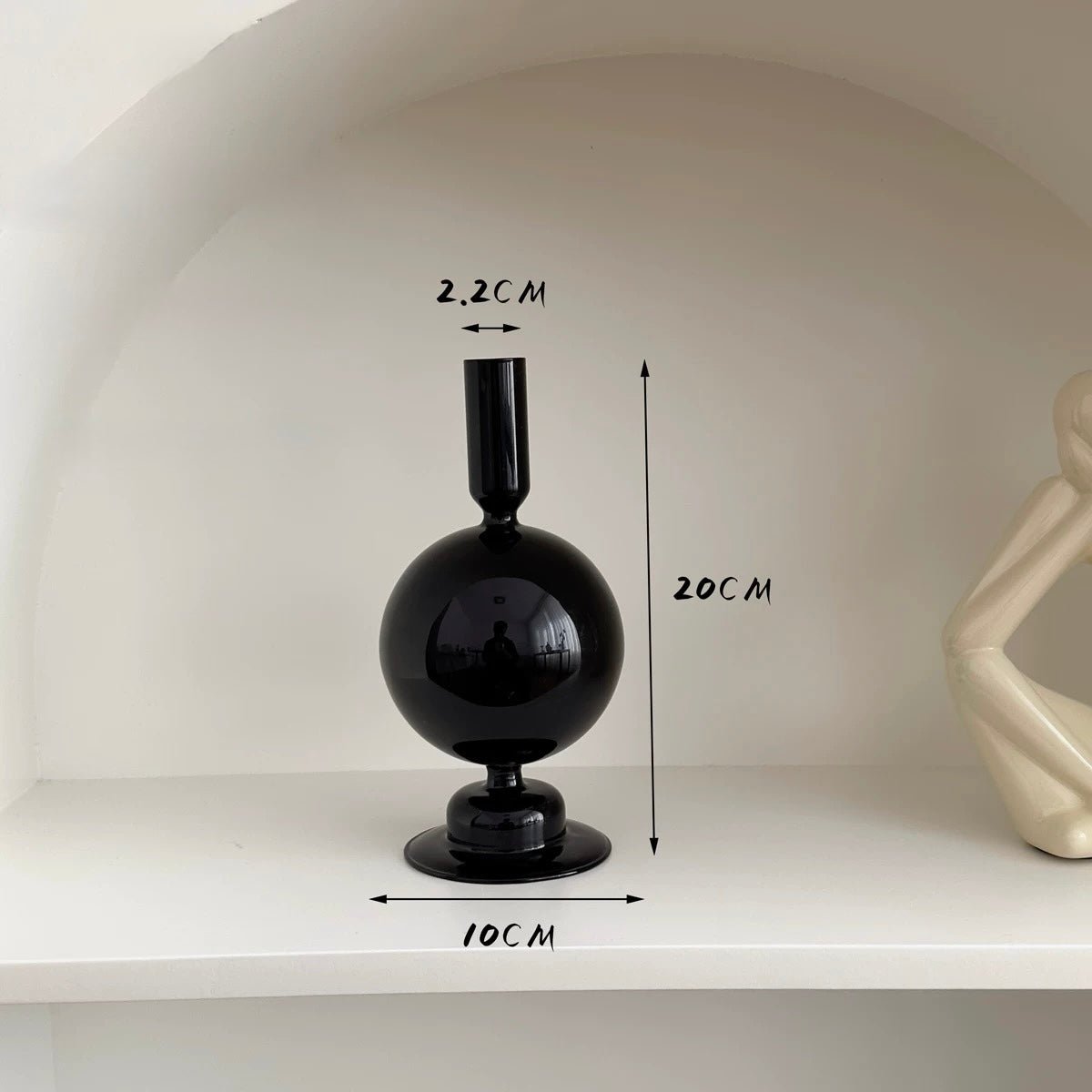 Black spherical vase on a white shelf with measurements indicated