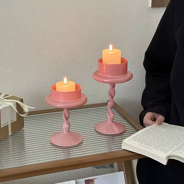Two pink candle holders with candles on a table next to a person reading a book.