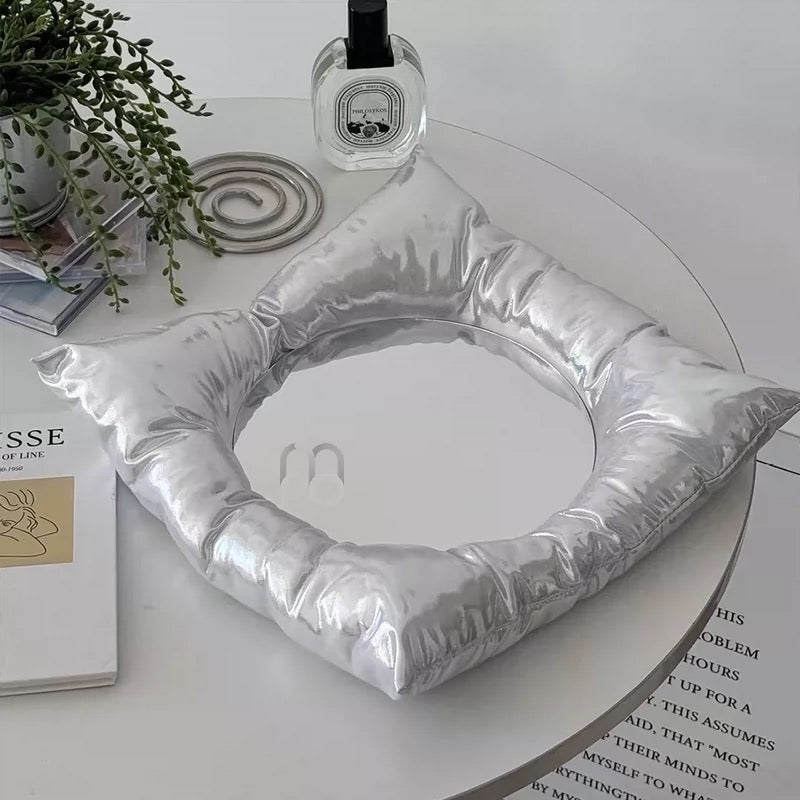 Silver cushion shaped like a mouth on a round table with books and a plant.