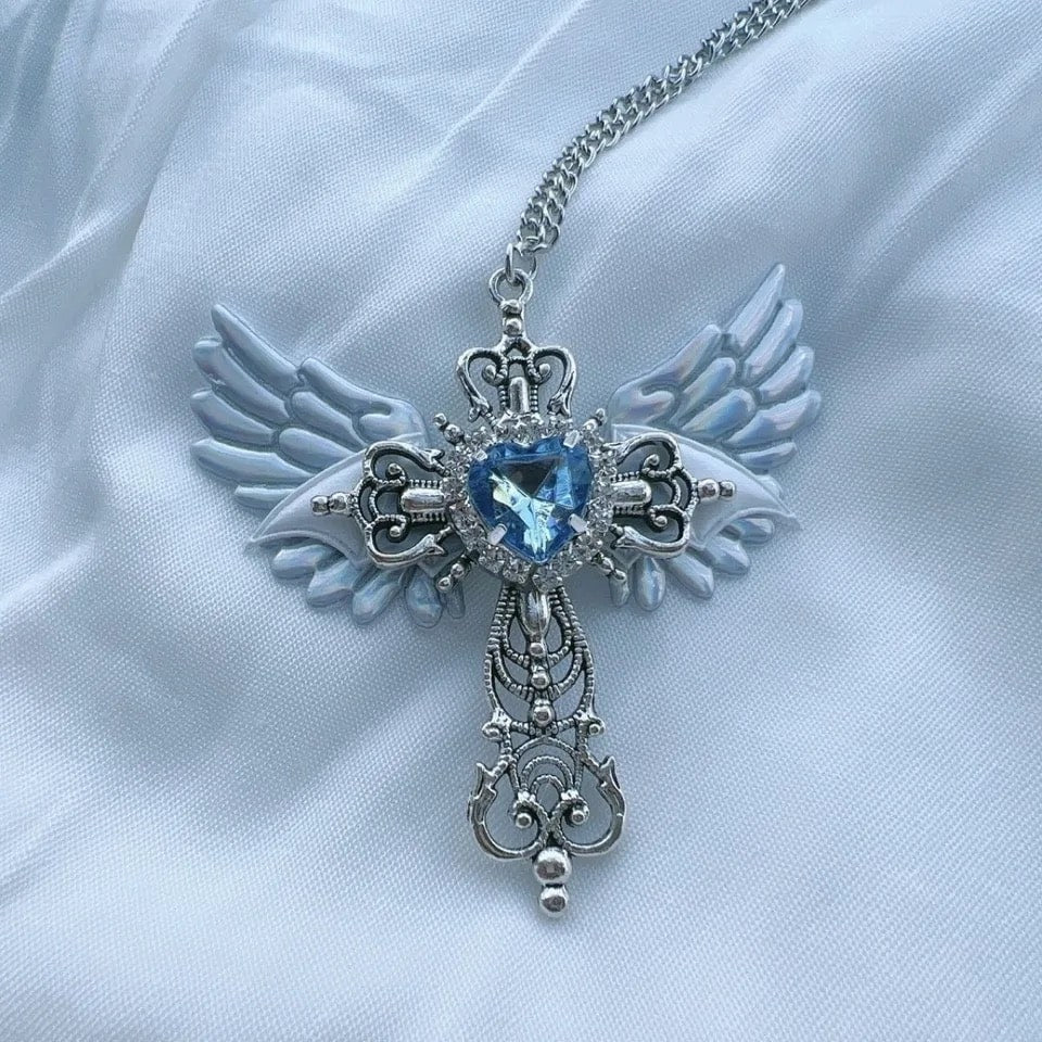 Blue heart crystal necklace with angel wings and cross pendant. Gothic-style charm perfect for women’s grunge and party outfits.