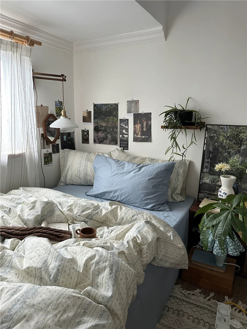 Light academia inspired bedding featuring blue floral stripes beside books and botanical decorations creating peaceful retreat indoors.