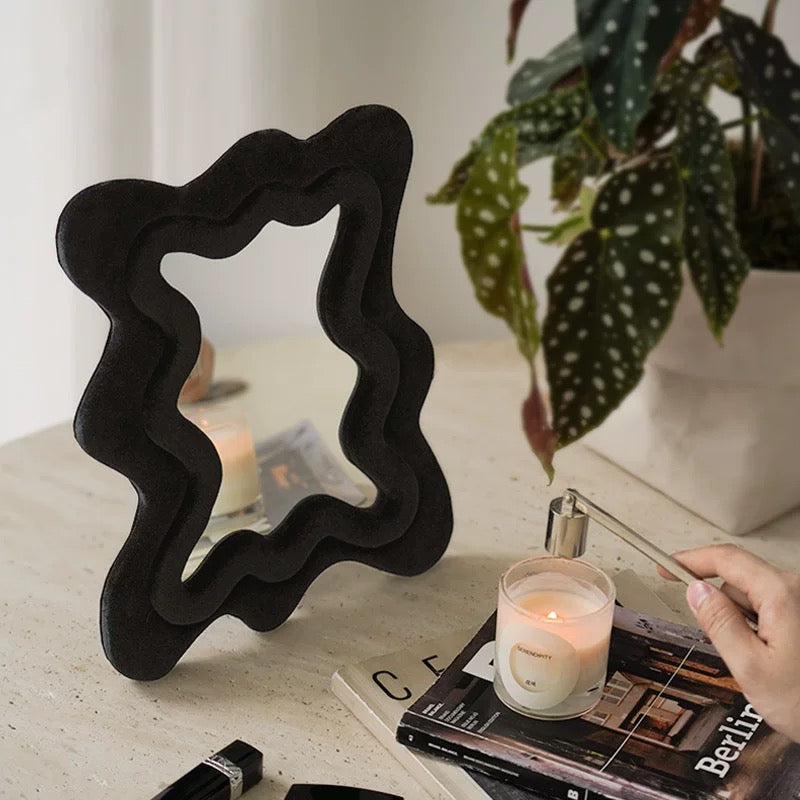 Black wavy mirror on a table with a candle and books
