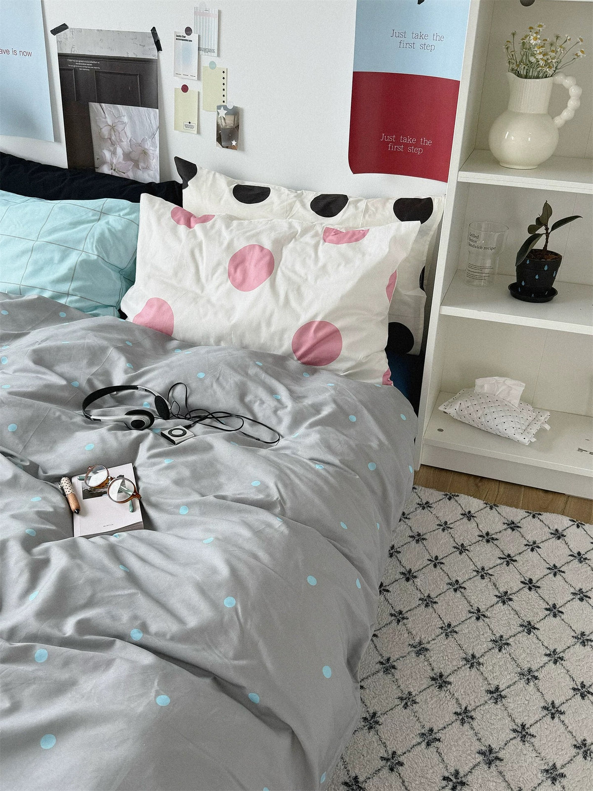 Gray and blue bedding shown beside a white shelf with layered patterned pillows.