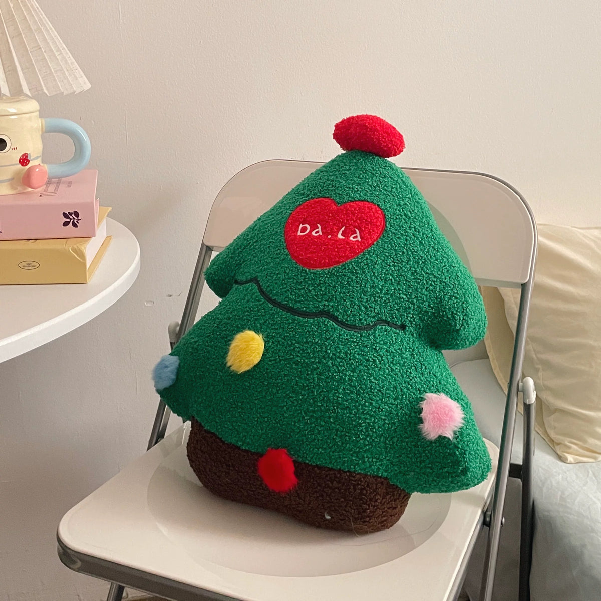 Green Christmas tree plush pillow with a red topper and colorful decorations on a chair