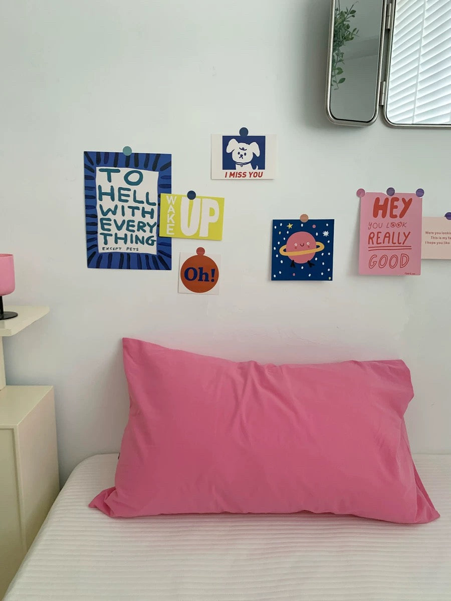 A pink pillowcase on a bed in a bedroom setting, with colorful decorative wall stickers pinned above it.