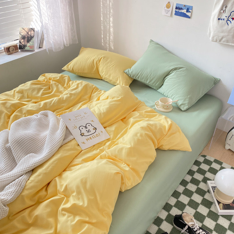 Bed with yellow bedding and green pillows in a room with a window and decor.