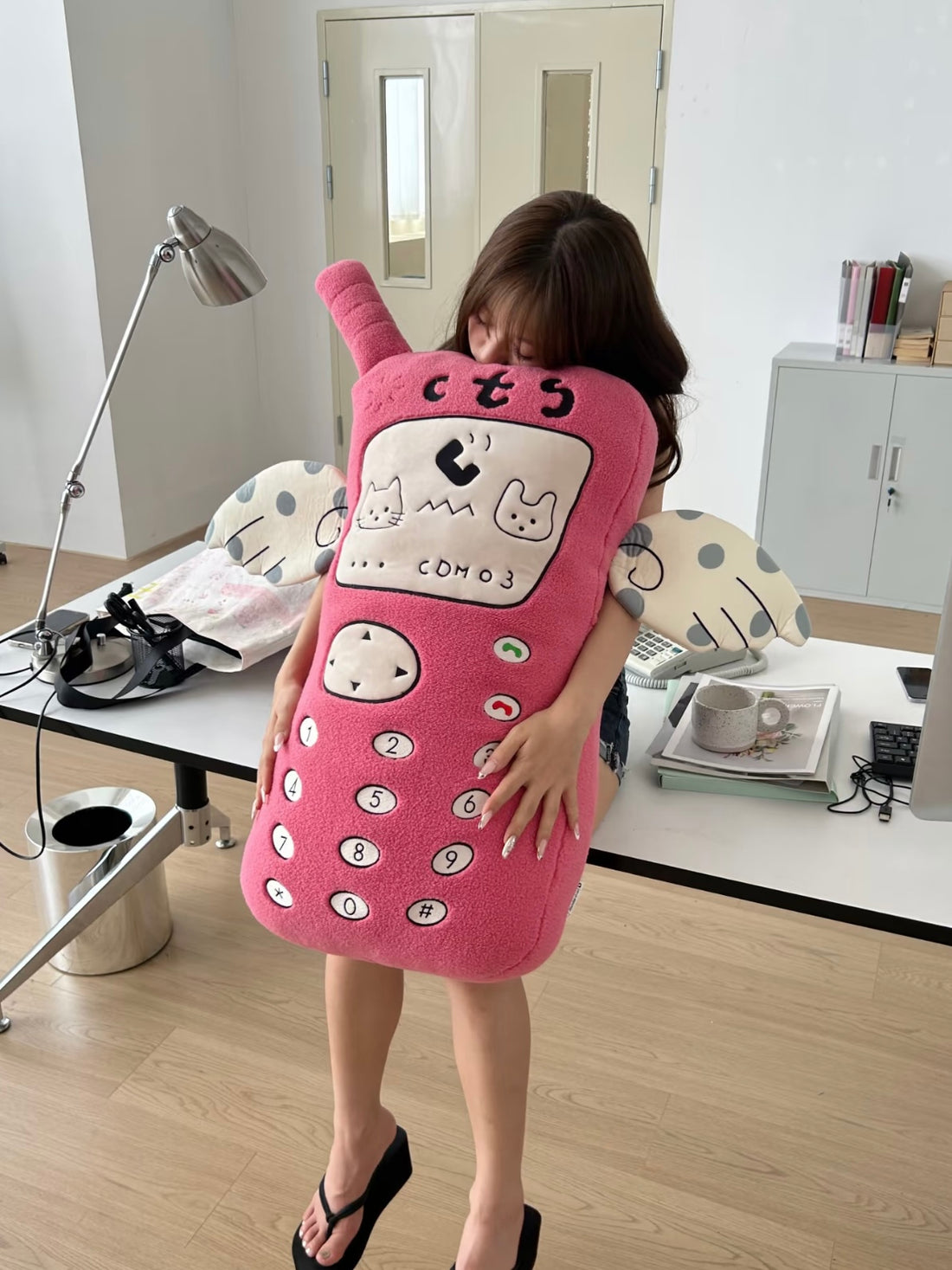 A pink phone Y2K pillow faces forward, with a raised antenna, embroidered screen details and pale spotted arms.