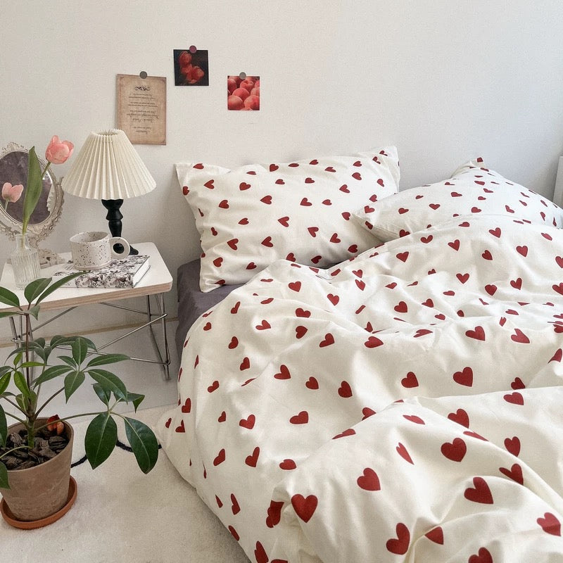 White heart print bedding set on a bed beside a pleated lamp, mirror and vase