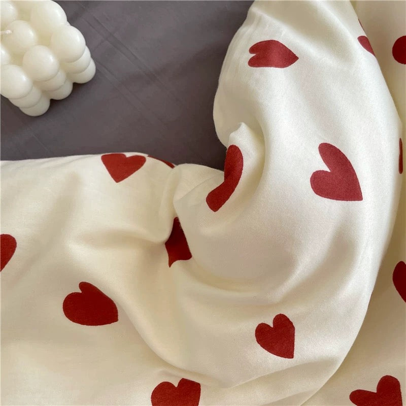 Close view of white cotton heart duvet cover with scattered red heart print and decorative candle