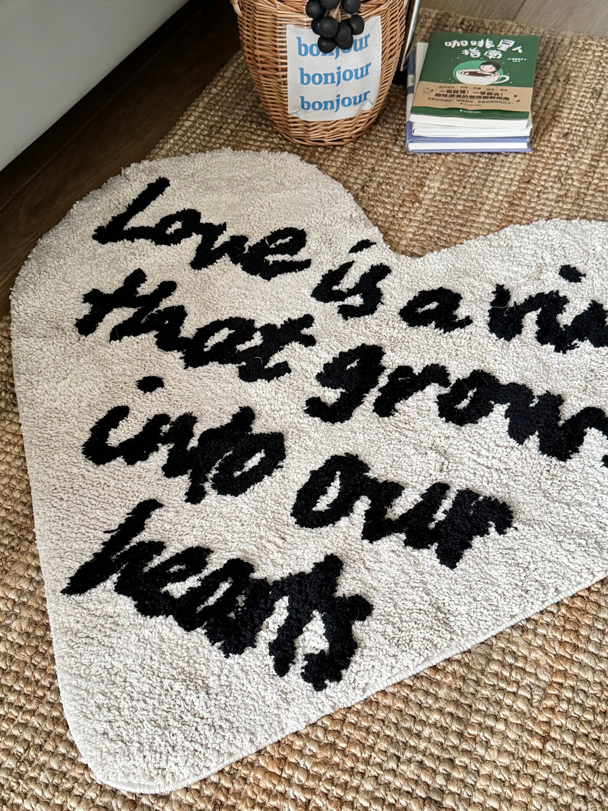 Cream heart shaped rug in a closer view, showing black raised lettering against the pale pile surface.
