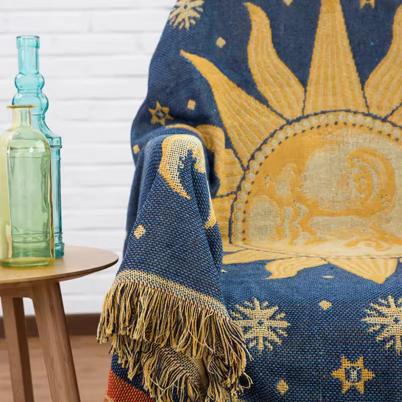 Decorative blue and gold throw blanket with celestial design draped over a chair, with two glass bottles on a table in the background.