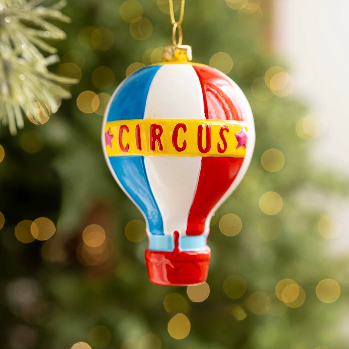A hot air balloon ornament has red, blue and white stripes with a yellow Circus band and pink stars.