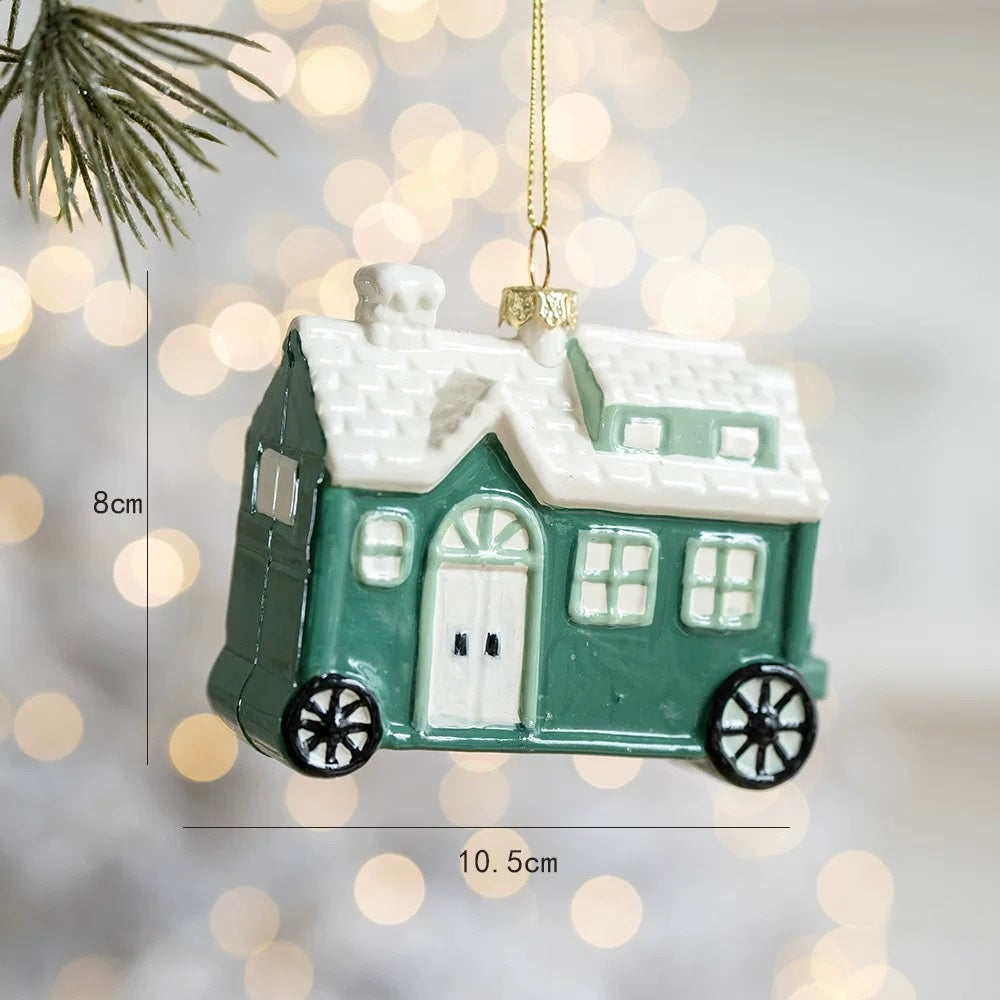 A house camper ornament has green walls, a white roof, a chimney and two black wheels with white spokes.