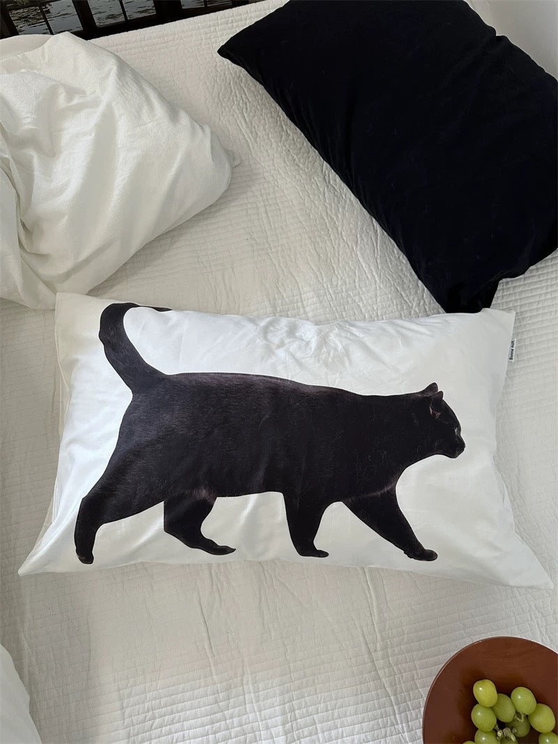 Pillow with a black cat design on a bed with white and black pillows.