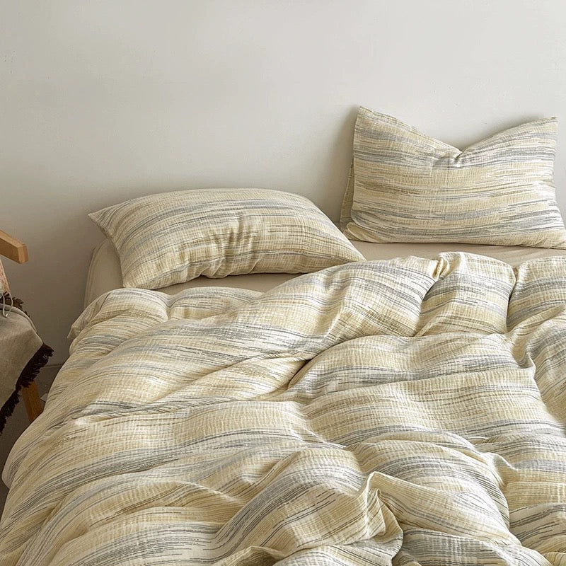 A bed made with a textured, crinkled cotton bedding set in a warm cream and muted gray colorway, featuring a duvet cover and two matching pillowcases against a plain off-white wall.