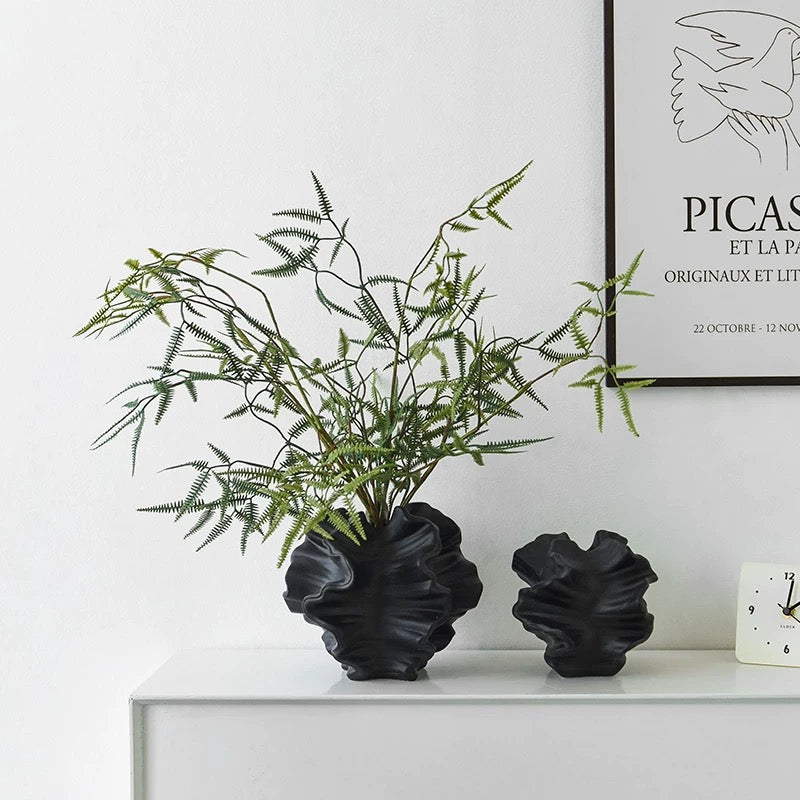 Decorative black vases with a plant on a white surface, framed artwork in the background.
