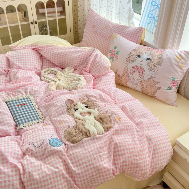 Pink checkered bedding set with cat design on a bed in a bright room.