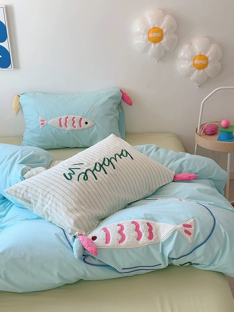 Close-up of playful fish embroidery on pastel blue duvet cover, showing textured 3D applique.
