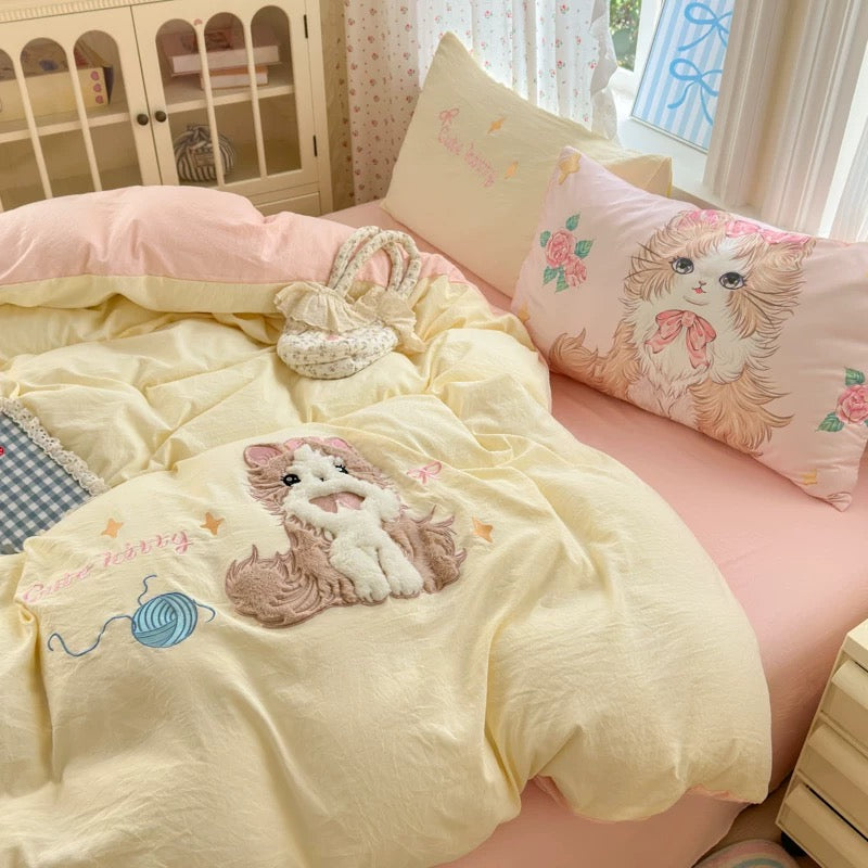 Bed with yellow comforter and pink pillows featuring cartoon cat designs in a bedroom setting.