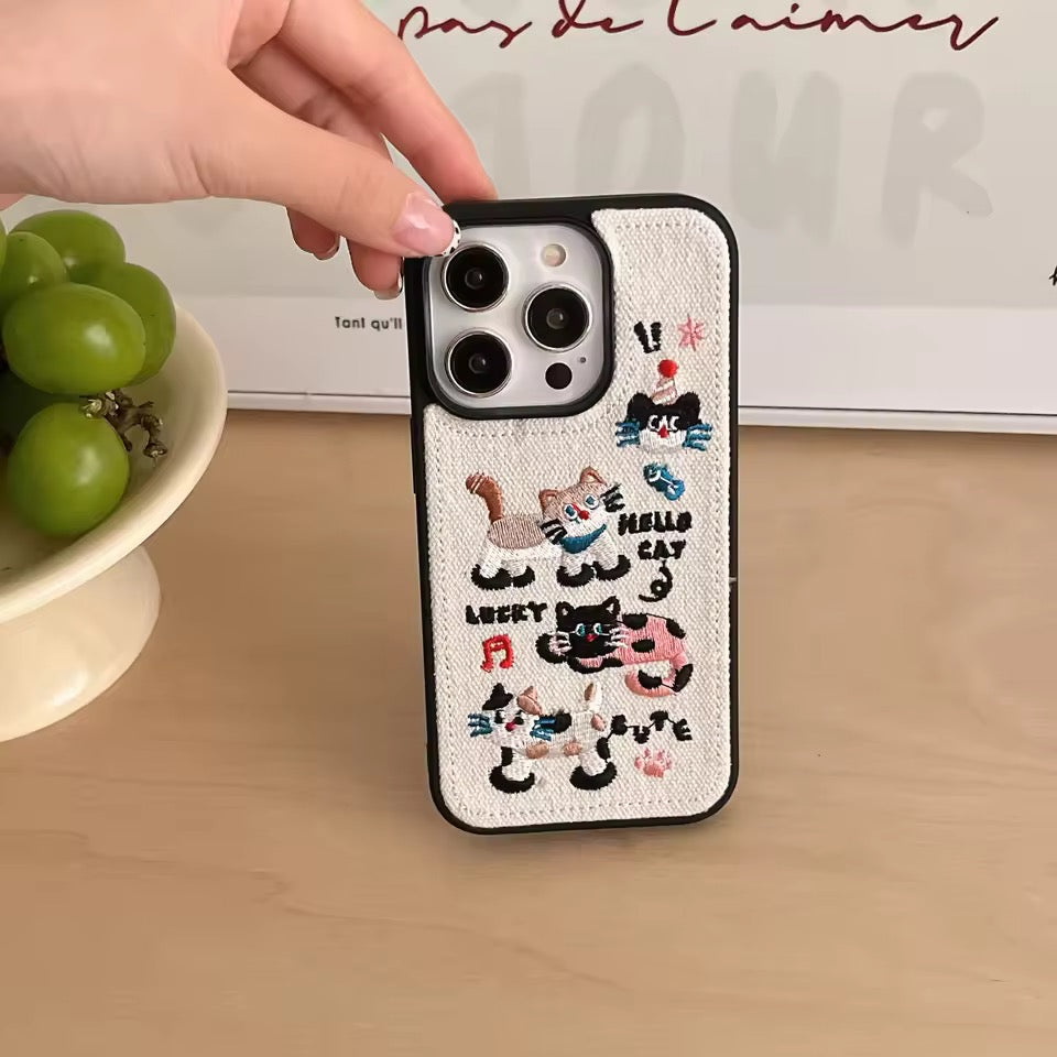 Phone case with cat designs held by a hand on a wooden surface.