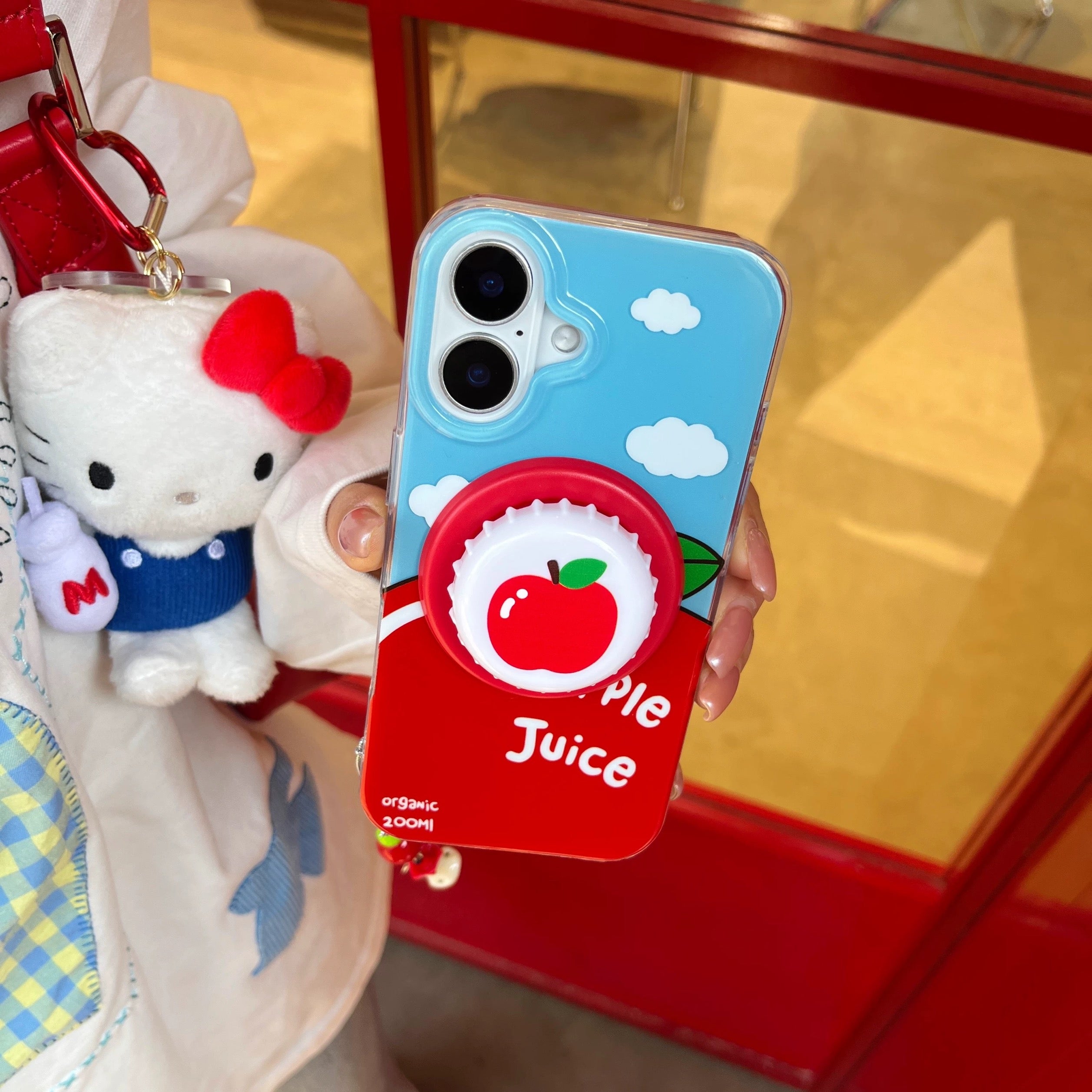 Phone case with apple juice design held by a person, with a plush toy in the background.