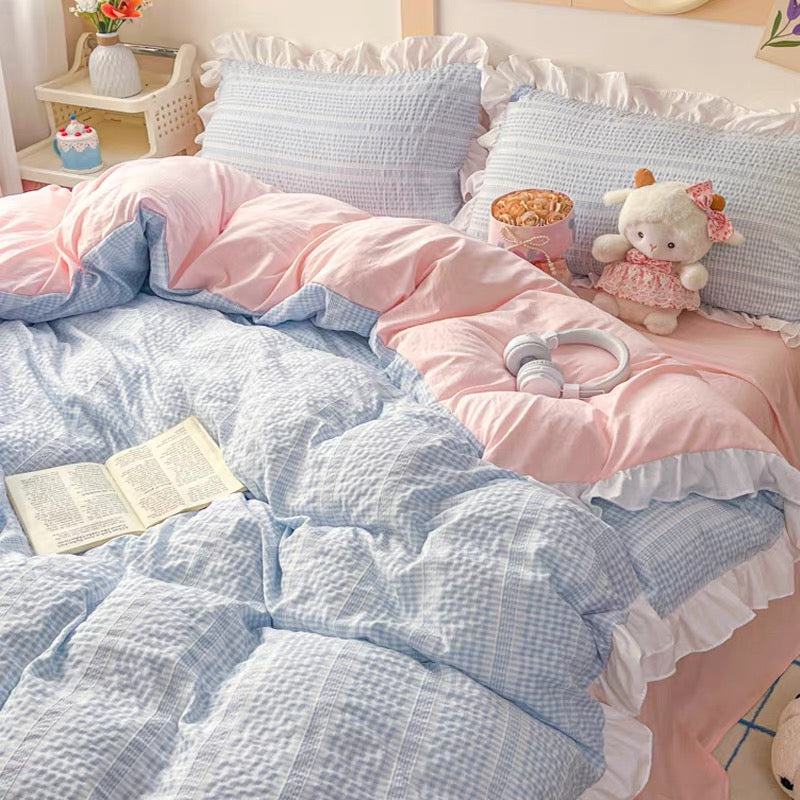 Bed with pink and blue checkered bedding, pillows, and a teddy bear.