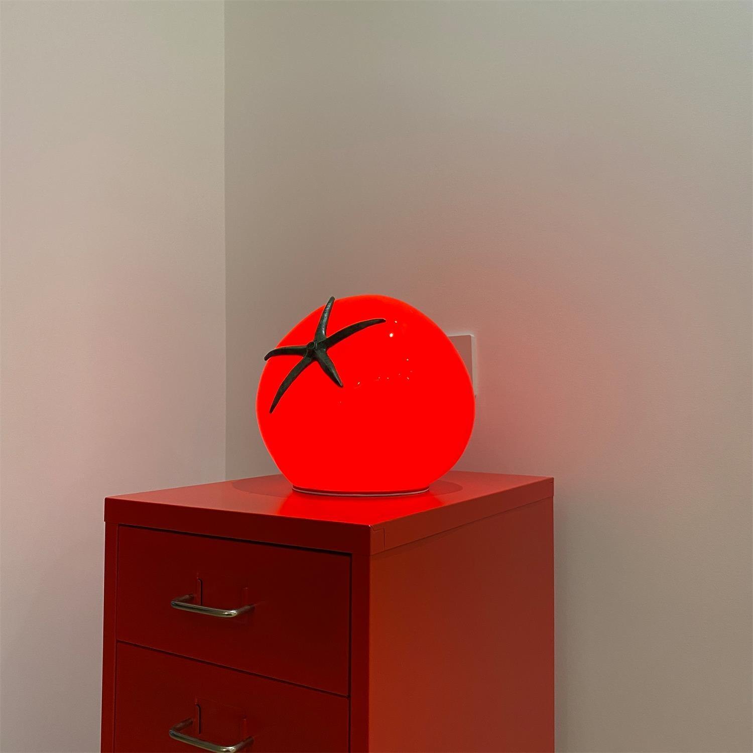 Red tomato-shaped lamp on a red cabinet against a plain wall