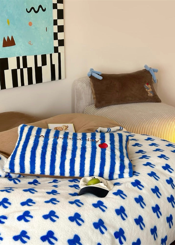 Bed with blue and white striped pillow and bow-patterned blanket, wall art in the background